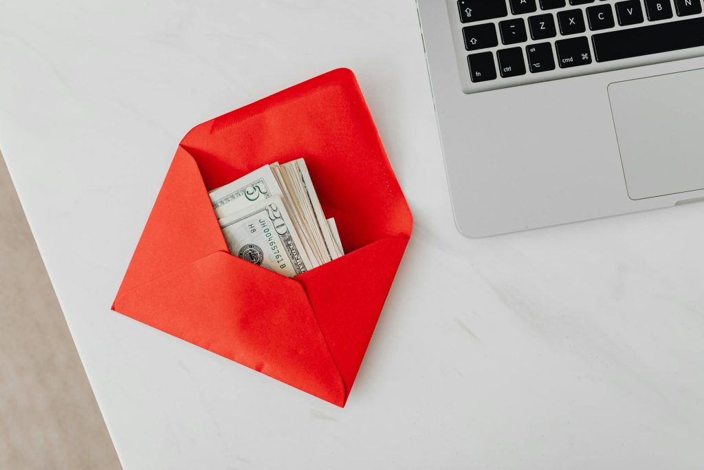 enveloppe rouge avec argent à côté d'un ordinateur portable