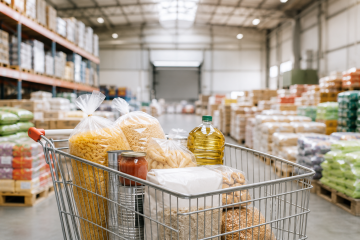 Chariot rempli de produits alimentaires en gros dans un entrepôt de grossiste alimentaire accessible aux particuliers, illustrant les achats en grande quantité à prix avantageux.